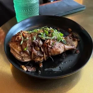 Seared protein dish with microgreens, nuts, and sauce.