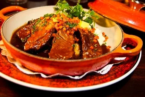 Braised meat with vegetables, herbs, creamy side in orange casserole.