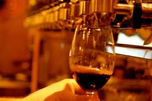 Hand holds glass as red wine pours from a dispenser.