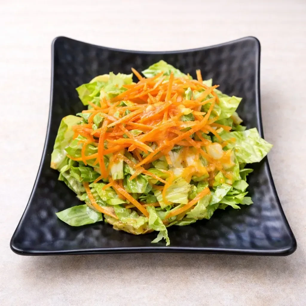 Green salad with shredded carrots and orange dressing, black bowl.