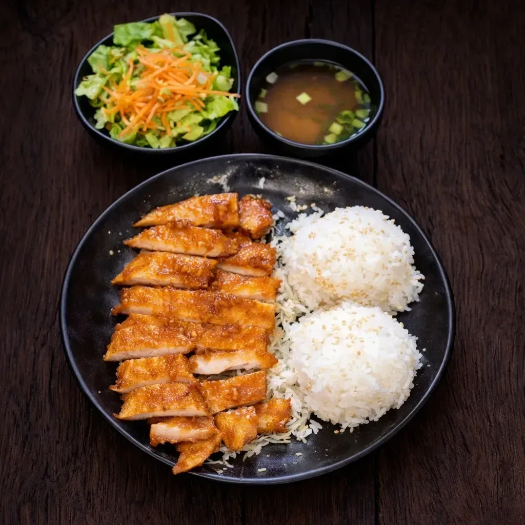 Japanese meal with sliced chicken, rice, salad, and miso soup.