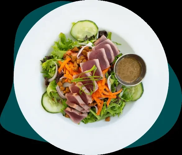 Seared tuna salad with vegetables and dressing on a white plate.
