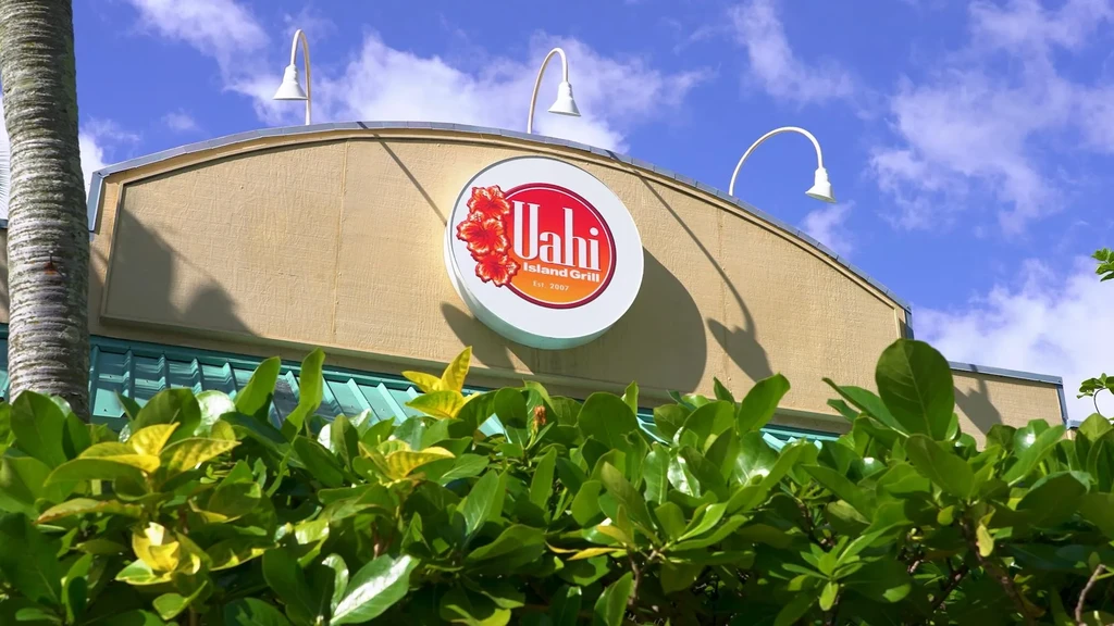 Circular "Uahi Island Grill" sign with hibiscus on a building.