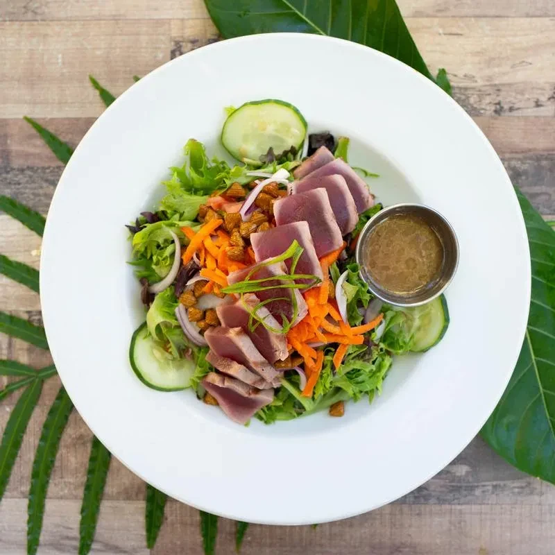 Seared tuna salad with mixed greens, vegetables, and dressing.