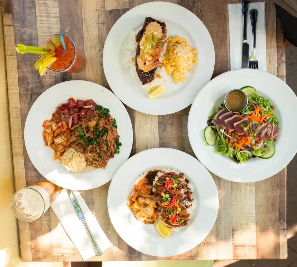 Four different food dishes and two drinks on a rustic wooden table.