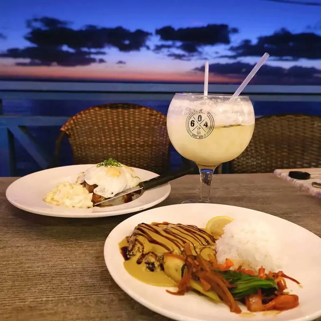 Food and drink on a table overlooking a vibrant sunset ocean.