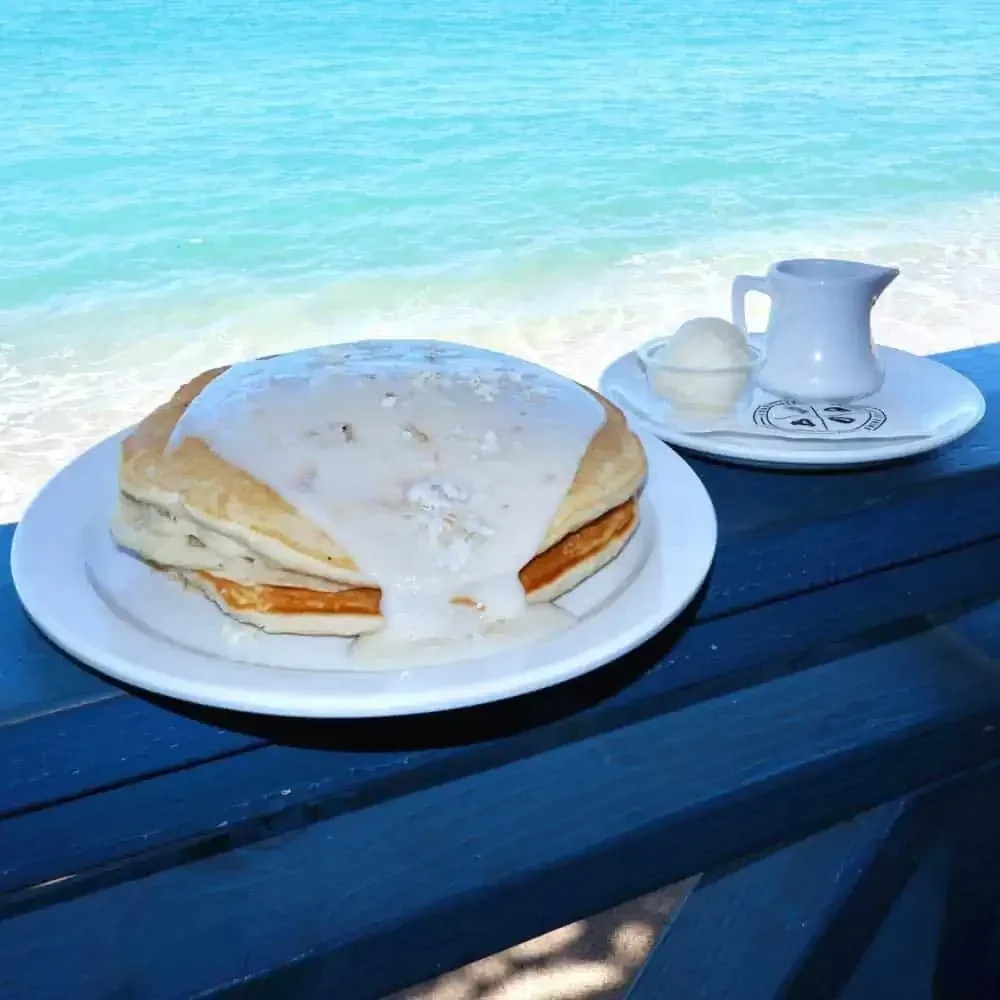 Stack of pancakes with cream and ice cream by turquoise ocean.