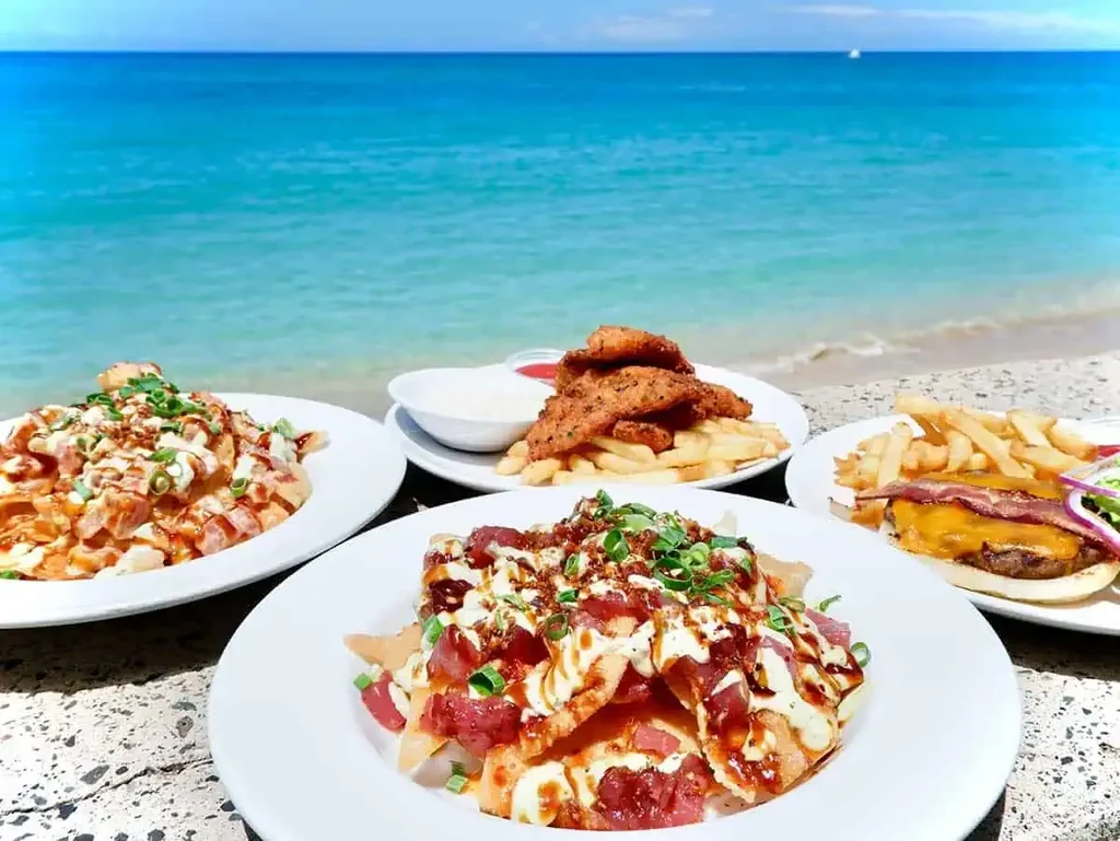 Poke nachos, burger, and fried food plates with an ocean view.