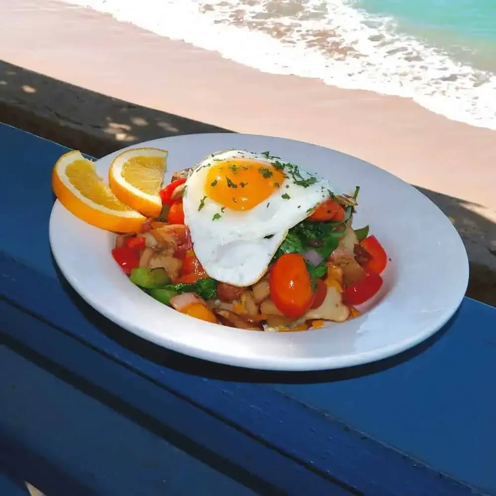 Sunny-side-up egg, vegetables, and fruit on a plate by the ocean.