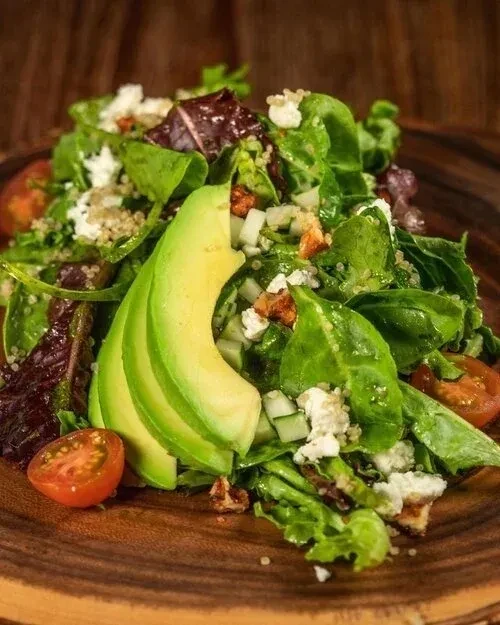 Fresh green salad with avocado, tomatoes, cheese, quinoa, and nuts.