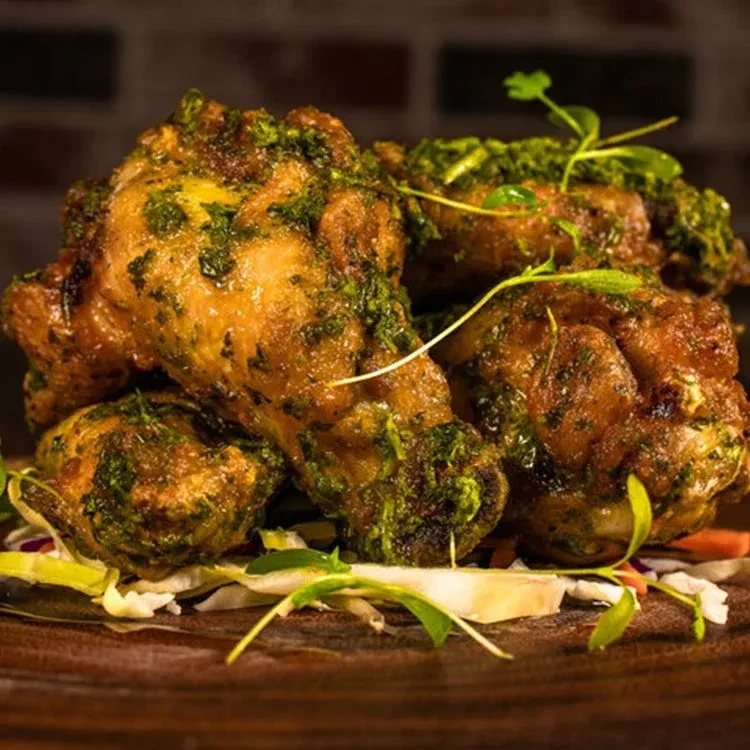 Crispy chicken pieces with green herb sauce, garnished on a wooden board.