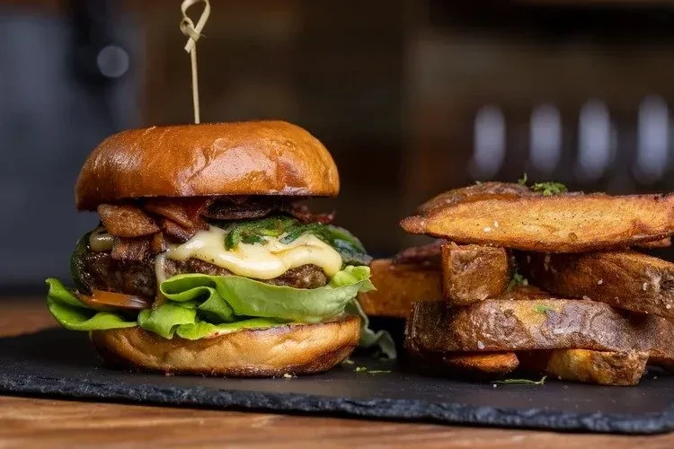 Gourmet burger and seasoned potato wedges on a slate board.