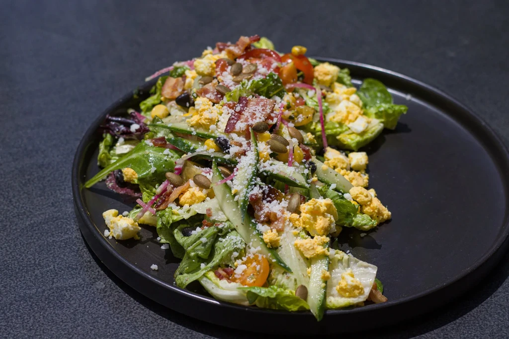 Brightly colored salad with greens, tomatoes, eggs, bacon, and cheese.