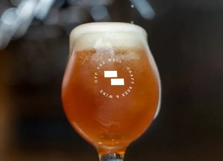 Amber craft beer in branded tulip glass with condensation, frothy head.