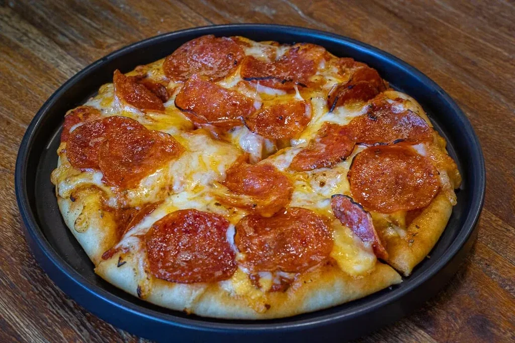 Freshly baked pepperoni pizza in a dark pan on a wooden table.