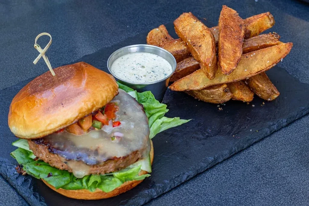 Gourmet burger with salsa, potato wedges, dipping sauce on slate.