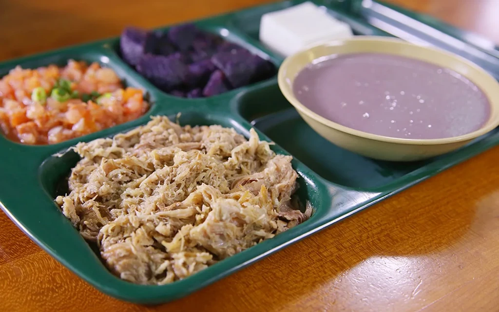 Compartmentalized tray with shredded meat, orange salsa, dark purple food, purple liquid.