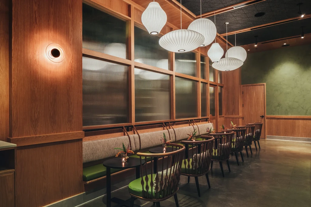 Contemporary restaurant with wood paneling, green booths, and pendant lights.