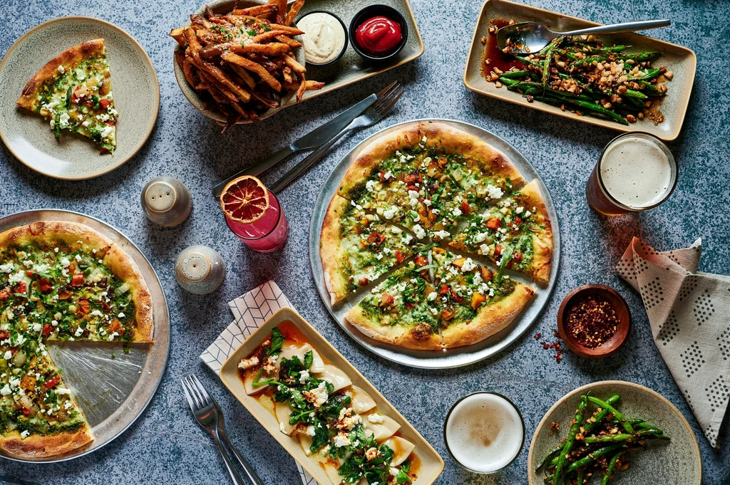 Overhead view of a diverse meal with pizzas, fries, and drinks.