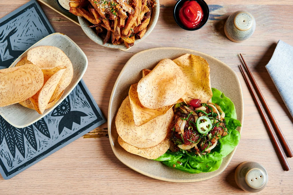 Overhead view of a wooden table with salad, taro chips, and condiments.