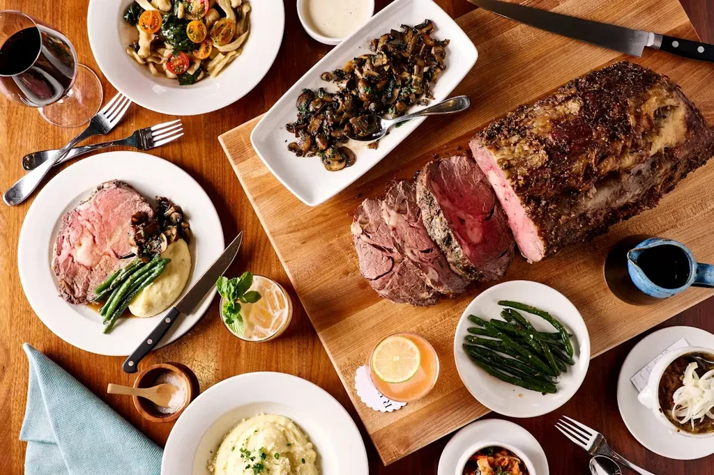 Dining table with a sliced prime rib roast, sides, and drinks.