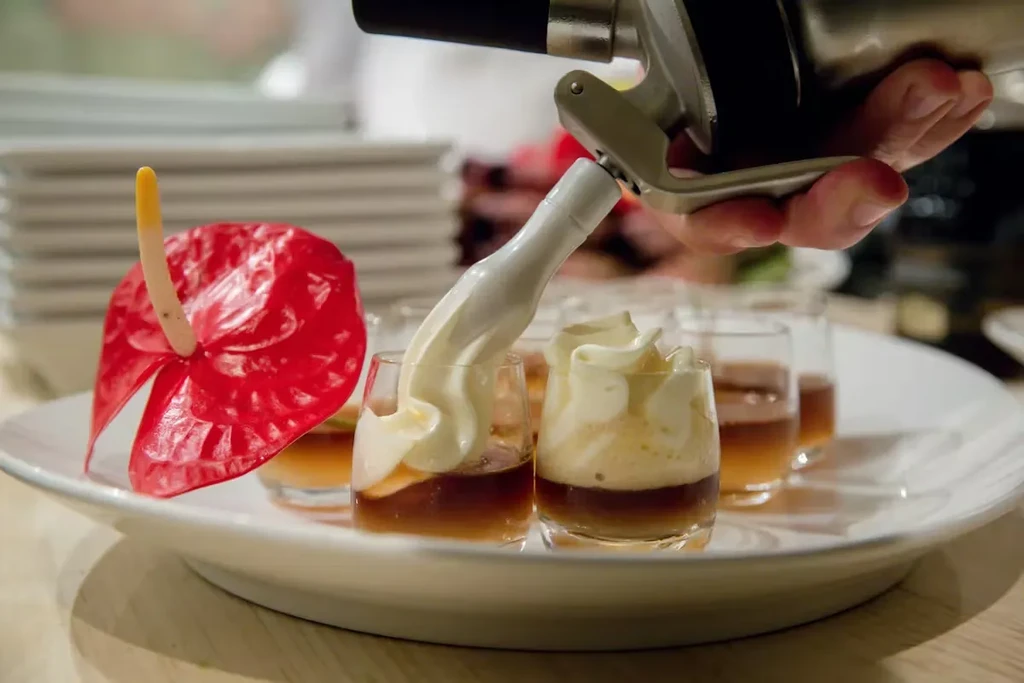 Hand piping whipped cream onto layered desserts on a platter.