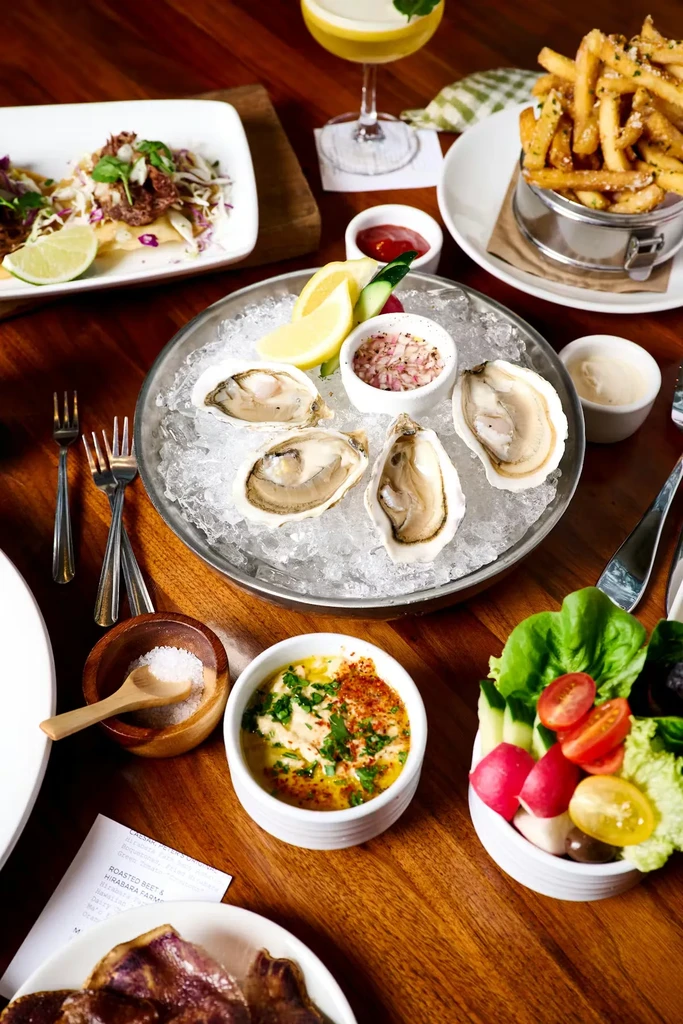 Overhead view: oysters, fries, salad, and cocktail on a wooden table.