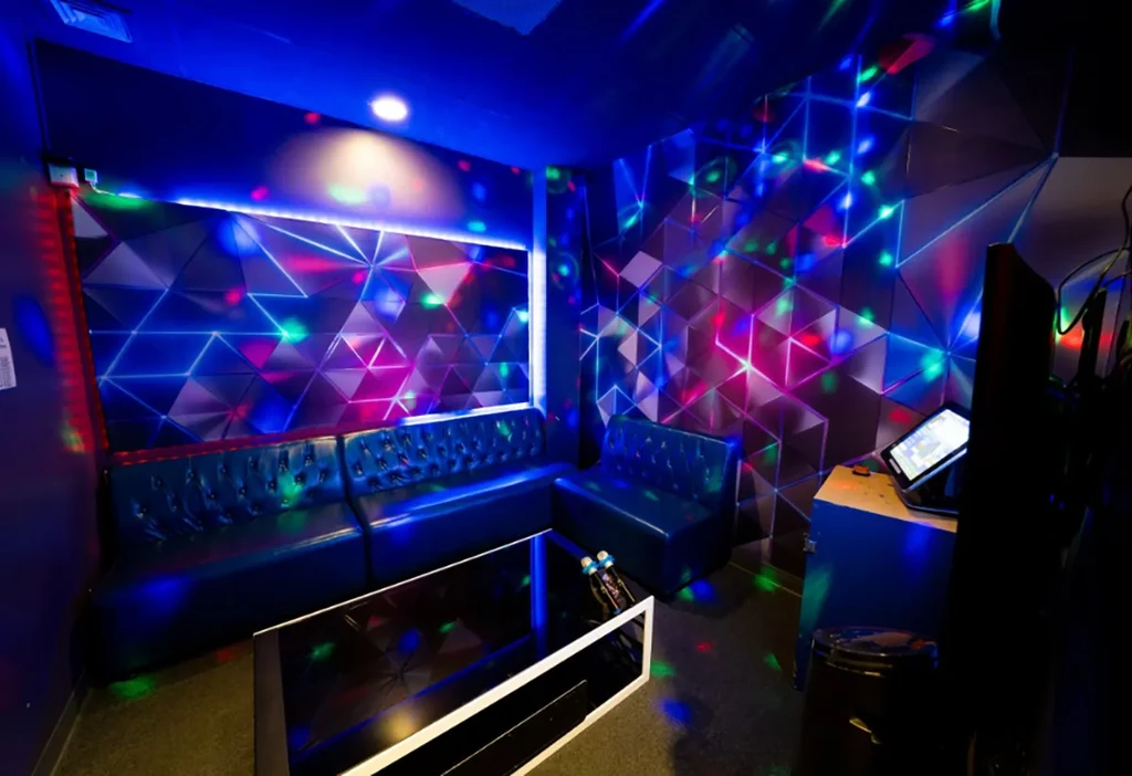 Geometric-patterned karaoke room with multi-colored lights and blue leather booth.