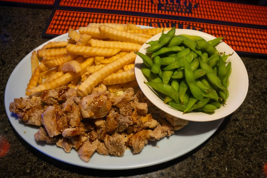 Fried chicken, crinkle-cut fries, and edamame on a bar table.