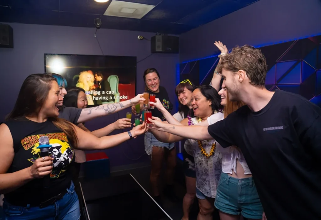 Young adults toast colorful shots while singing karaoke.