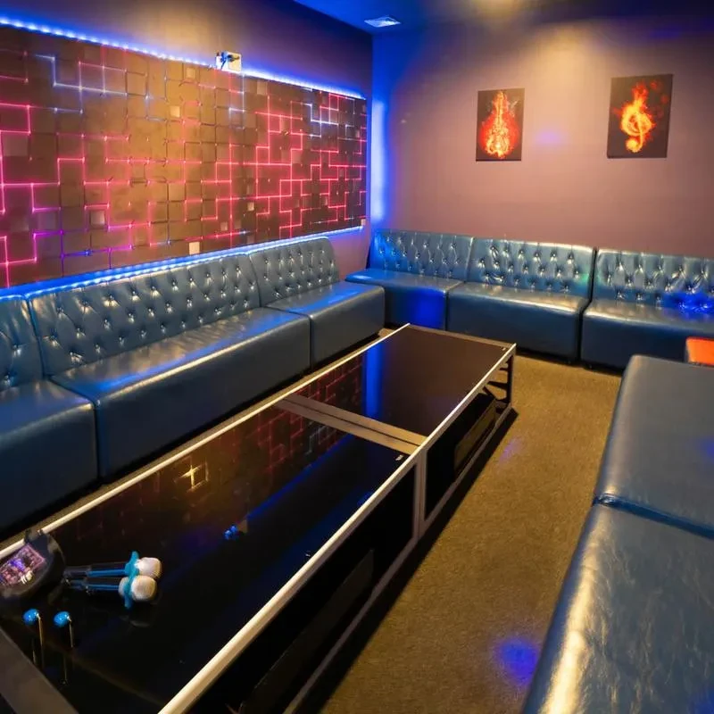 Modern karaoke room with blue sofas, glowing grid wall, and microphones.
