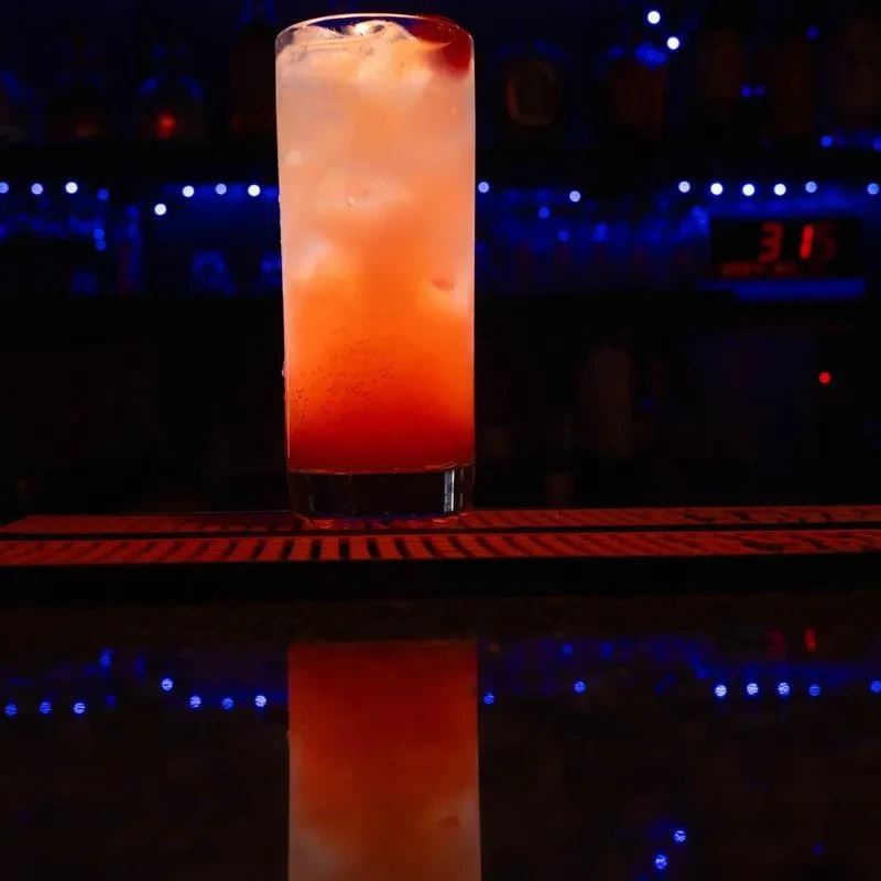 Layered red-orange and white cocktail with ice on a reflective bar.