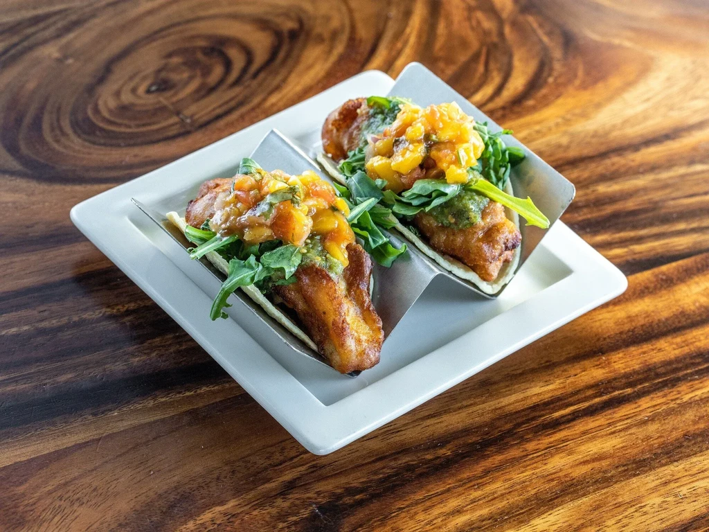 Two tacos with crispy filling, orange salsa, and green toppings.