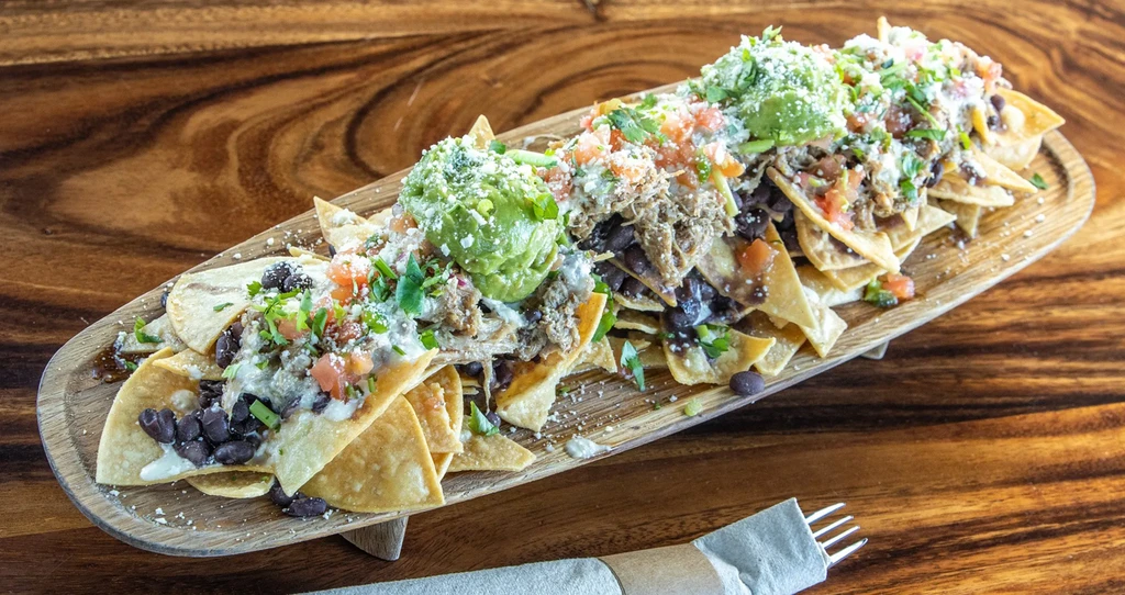 Loaded nachos with meat, beans, salsa, guacamole, cheese on a board.
