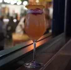 Peach cocktail with frothy pink top, dried citrus, in a stemmed glass.
