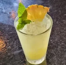Tall glass with pale green cocktail, crushed ice, pineapple, and mint.