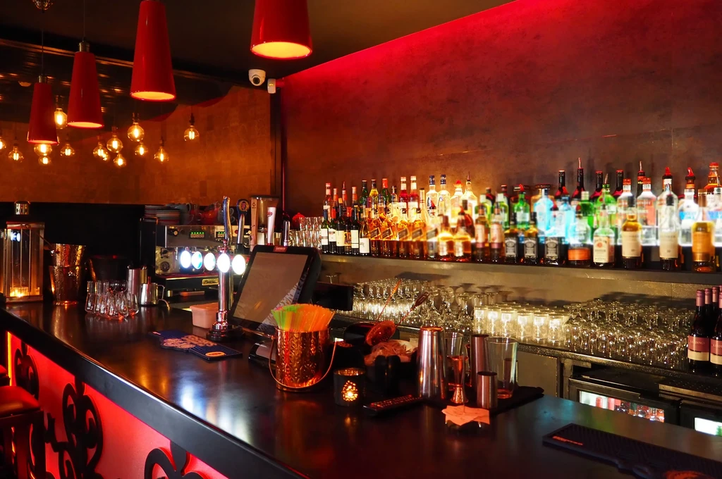 Well-appointed bar with liquor bottles, glassware, and red lighting.