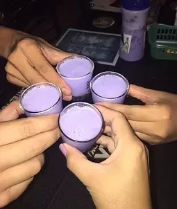 Four hands toast purple shot glasses in a dark bar.