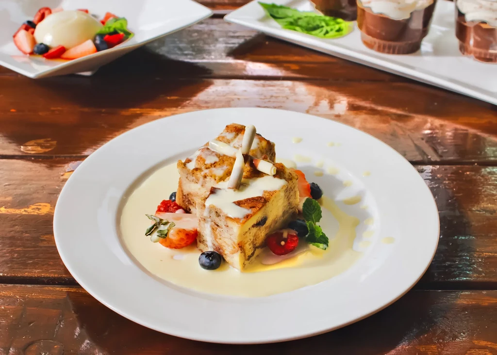 Plated baked dessert with berries, mint, white glaze, yellow sauce on wood.
