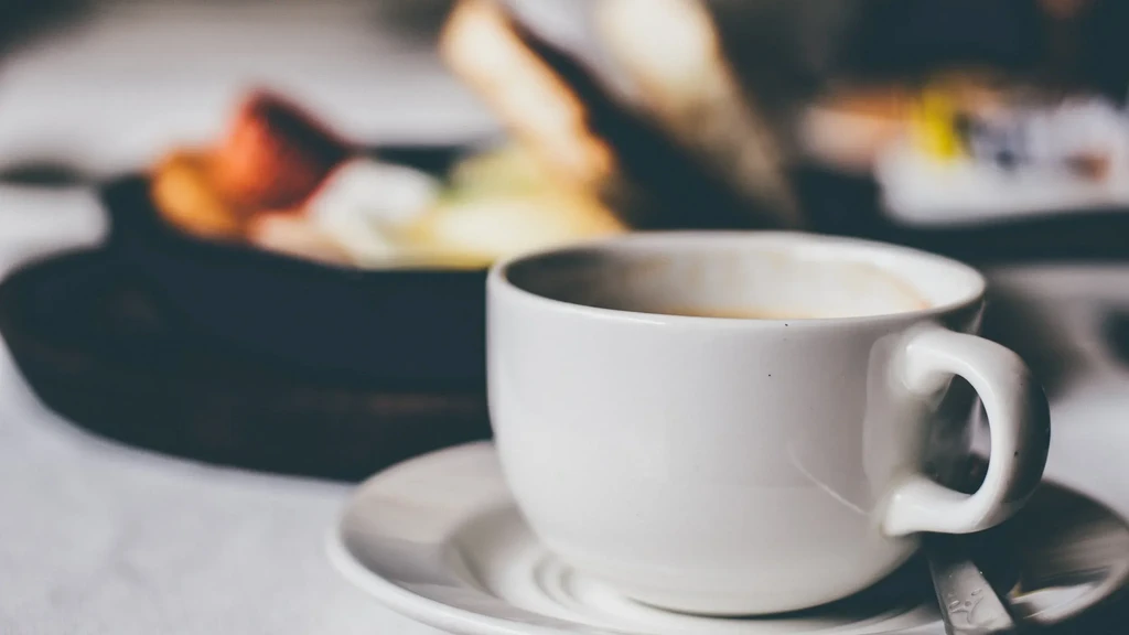 White coffee cup with partially consumed drink, saucer, and spoon.