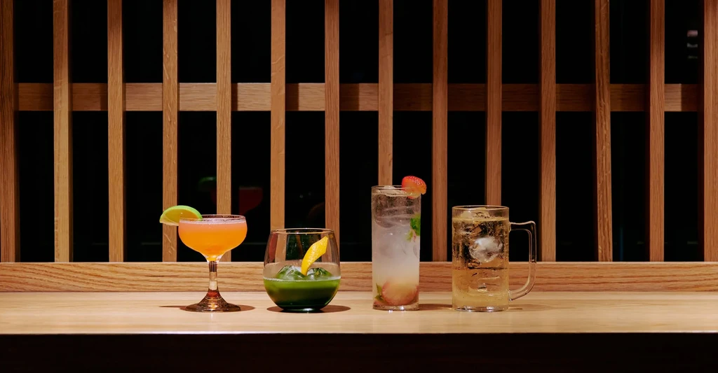 Four colorful cocktails in different glasses lined up on a wooden bar.