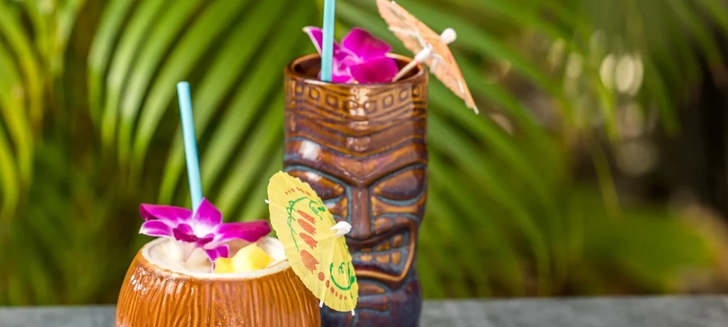Two tropical cocktails in unique mugs garnished with purple orchids.