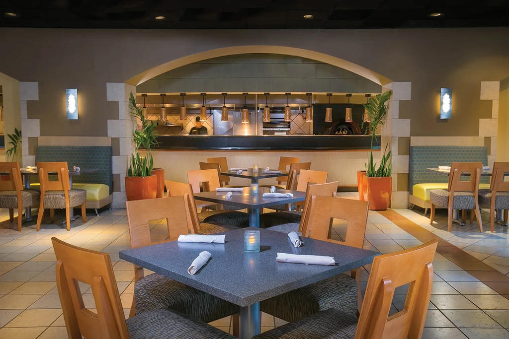 Contemporary restaurant interior with dining tables, booths, and visible pizza oven.