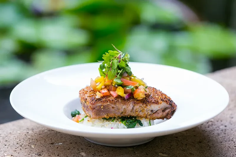 Seared tuna with bell pepper salsa, rice, and greens outdoors.