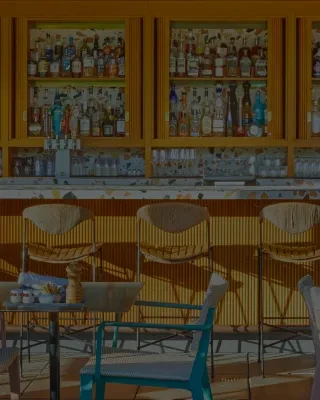 Modern bar with colorful terrazzo counter, alcohol bottles, and chairs.