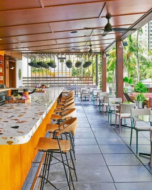 Modern tropical restaurant/bar with a terrazzo bar, wooden panels, and palm trees.