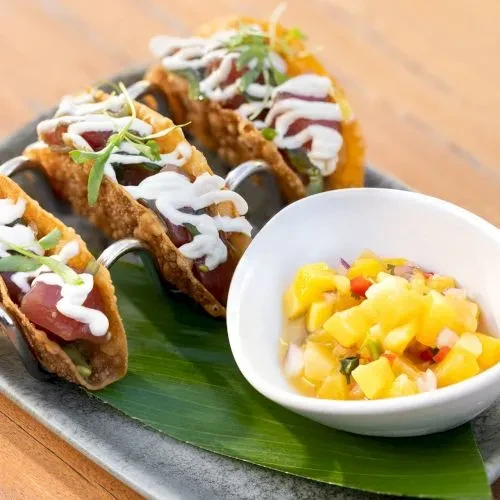 Three crispy tuna tacos with white sauce and mango salsa on a plate.