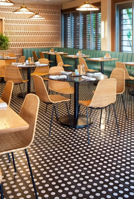 Empty, upscale restaurant interior with wicker chairs, teal booth, and polka-dot floor.