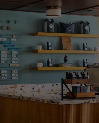 Modern coffee shop counter with yellow shelves, products, and a menu.