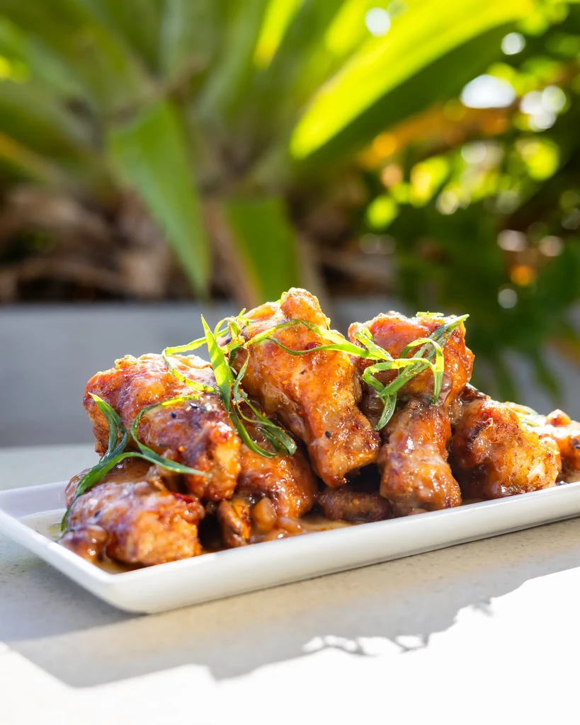Golden-brown chicken wings with glistening sauce and green onions on plate.